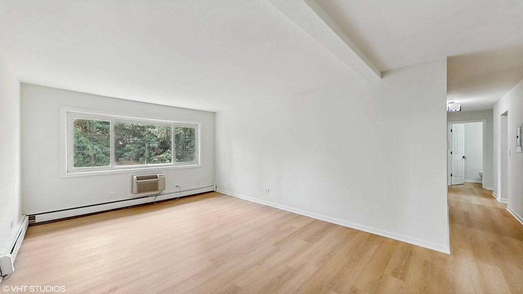 A room with wooden floors and white walls, with a window showing greenery outside.