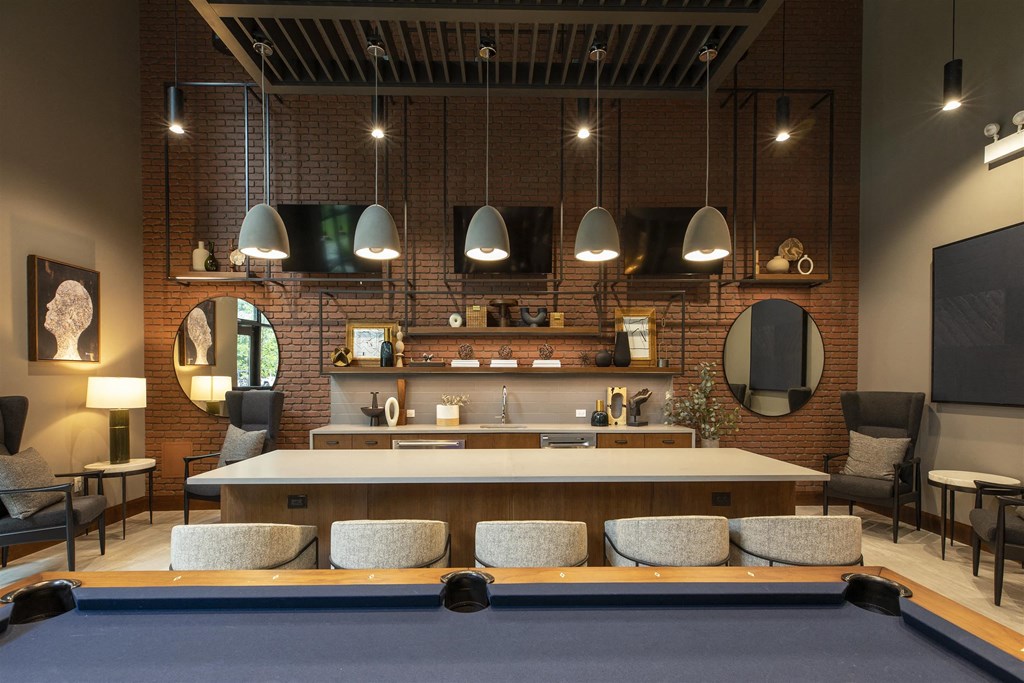A pool table is in the middle of a room with a brick wall and a bar area.