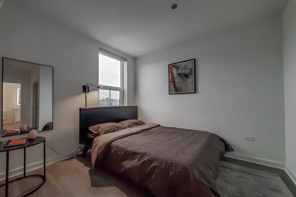 A bedroom with a bed, a table, and a mirror.