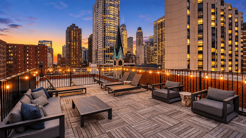 A rooftop patio with a table and chairs overlooking a city skyline at dusk.