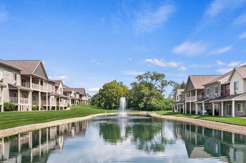 A serene scene of a pond with a fountain in the middle of a row of houses.