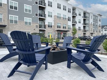 a patio with blue chairs and a fire pit in front of an apartment building at Enclave Crystal Lake Townhomes and Apartments, Crystal Lake, 60014