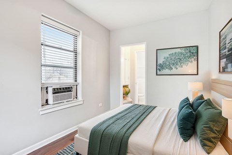 A bedroom with a bed, a window with blinds, a lamp, and a painting on the wall.