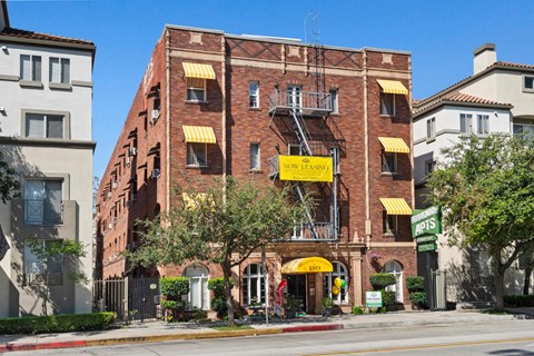 A red brick building with a yellow awning and a sign that says Now Leasing at Brookmore Pasadena apartments.
