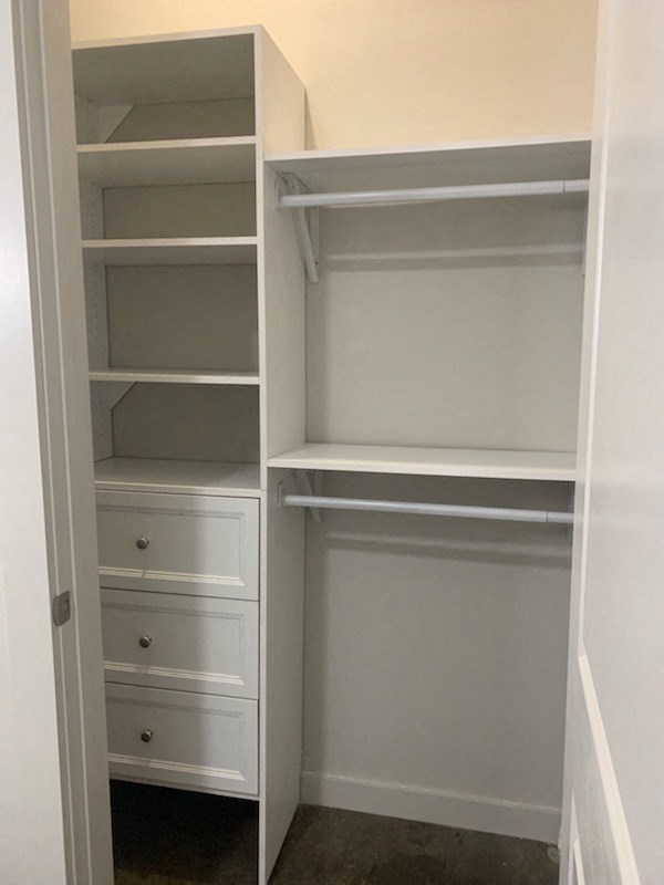 Walk-in closet in State Street Flats one bedroom apartment in Nashville with white built in shelving, dresser, and closet rods.