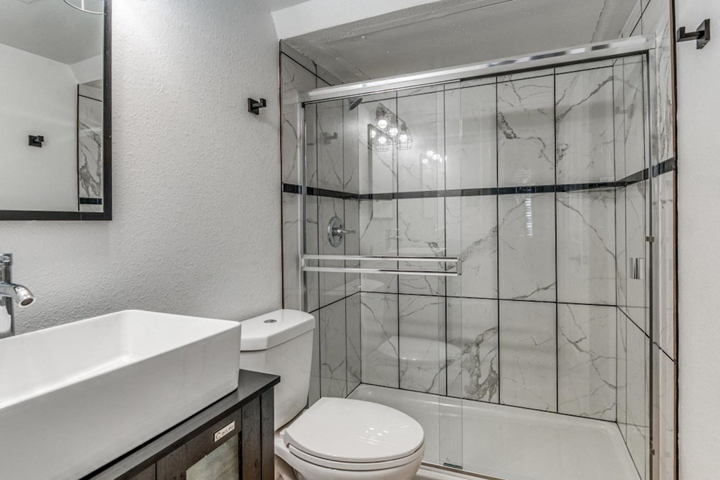 Fusion Fort Worth apartment renovated bathroom with veined marble tile, clear glass sliding door, and chrome trim on large shower.