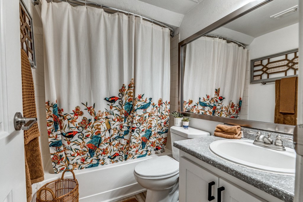 Renovated Bathroom in Fusion Fort Worth apartment in Haltom City. Teal, Red, and Camel colored birds embroidered on shower curtain in large bathtub.