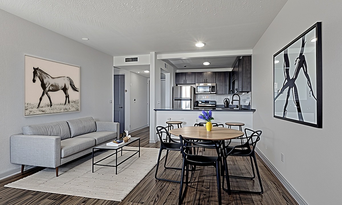 A living room with a grey couch and a painting of a horse on the wall.