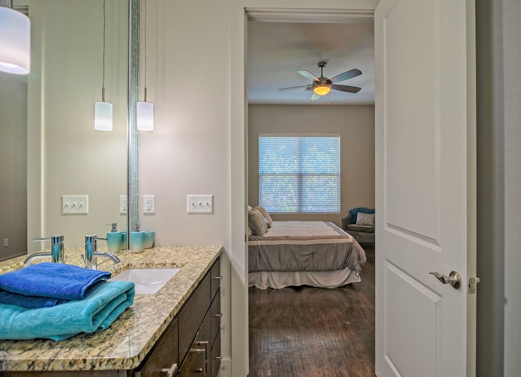 View from bathroom to bedroom in State Street Flats one bedroom apartment in Nashville. Bathroom vanity has granite countertop and double wide mirror.