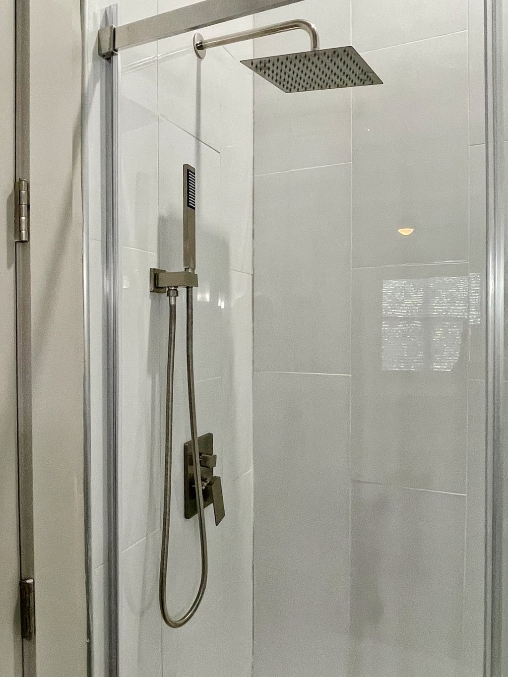 Shower in State Street Flats one bedroom apartment in Nashville with sliding glass doors, large white modern tiles, and dual rain shower head.