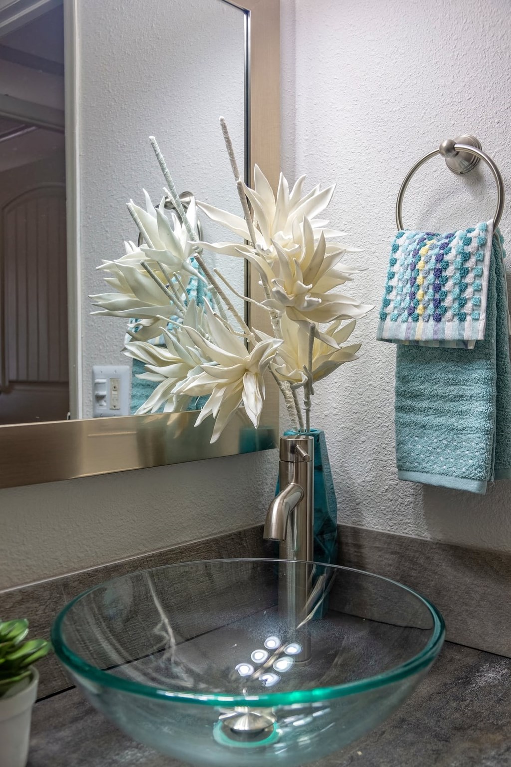 Bathroom sink in the Retreat at Indian Lake one bedroom apartment in Hendersonville with glass basin sink and chrome framed mirror.