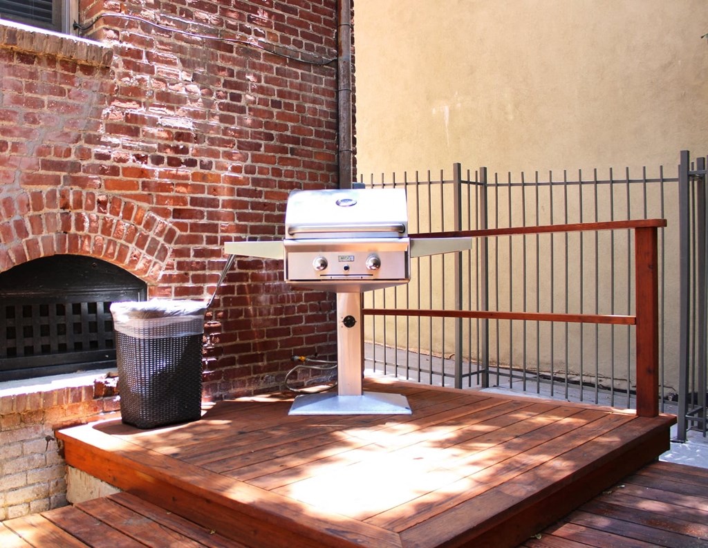 Brookmore Pasadena ca apartments grilling station with a stainless steel grill and trash can on a stained wood deck with railing and brick wall.