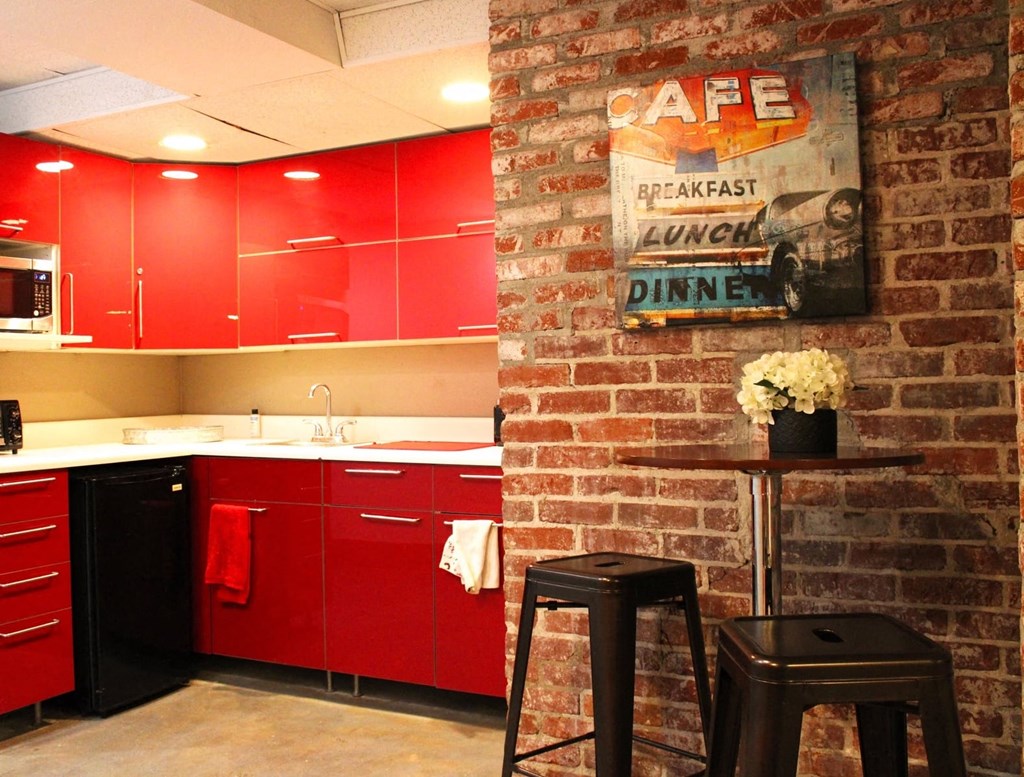 Brookmore apartments community kitchen with red cabinets, dishwasher, and microwave, and sitting area with small bar table and two black stools.