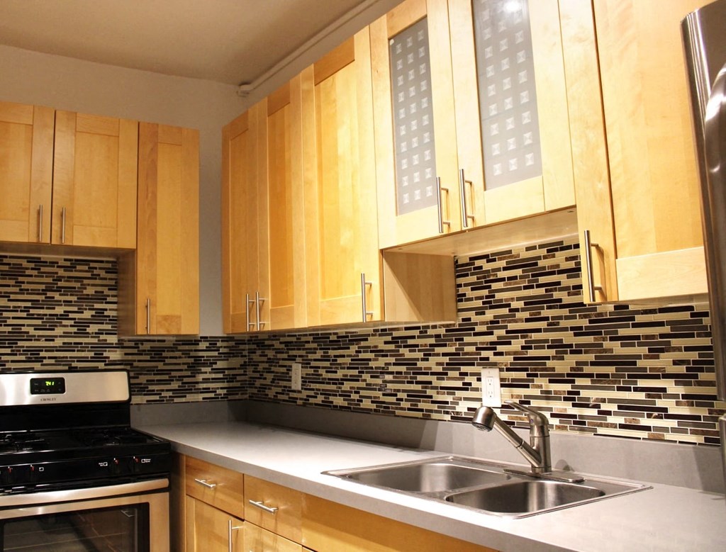 A kitchen in Brookmore apartments in Pasadena ca with modern, honey wood cabinets, multicolored tile backsplash, six burner gas stove, and dual sink
