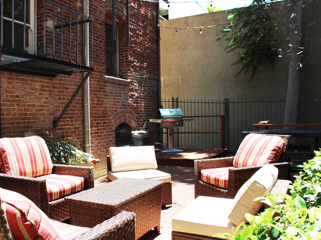 Brookmore Pasadena ca apartments back patio next to brick wall. Stained wood deck with cushioned wicker patio furniture and grill.