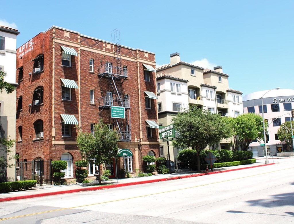 Street view of Brookmore apts in Pasadena CA. Four story brick building with striped awnings, fire escape, and "now leasing" sign.