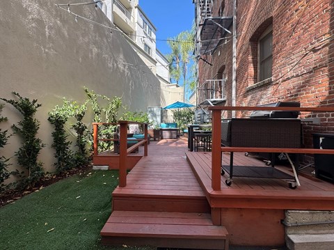 Brookmore Pasadena ca apartments back patio surrounded by greenery and brick wall with wicker patio furniture, stained wood deck, and grilling station.