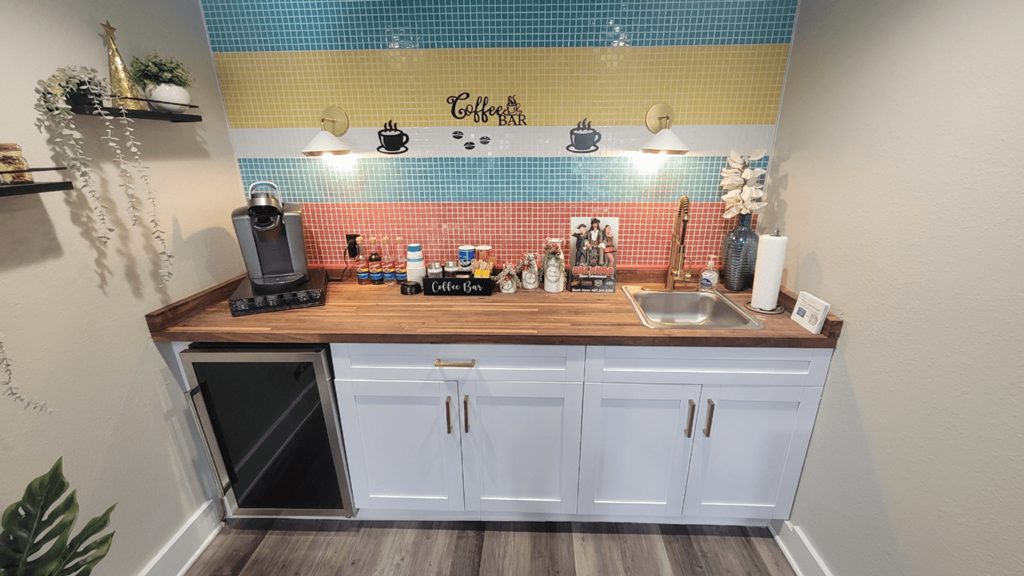 Fusion Orlando apartments coffee bar with butcher block counter, white cabinets, colorful tile wall, and Keurig with coffee pods and cups.