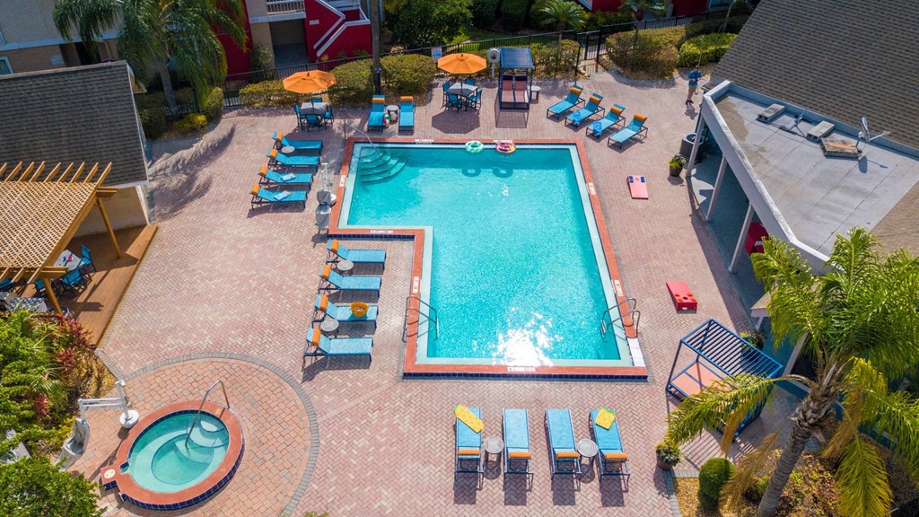 Aerial view of L-shaped community pool at Fusion Apartments in Orlando, FL. Pool is next to pool house, wood trellis, and round hot tub.