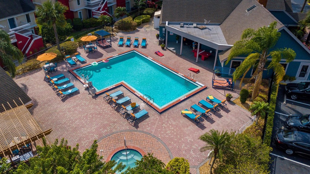Aerial view of L-shaped community pool at furnished Fusion Apartments in Orlando, FL. Pool is surrounded by blue lounge chairs and palm trees.