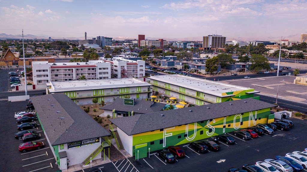 Aerial view of four Las Vegas Fusion apartment buildings in a square around amenities house and community pool in desert landscape.