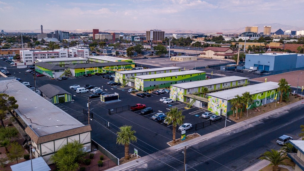Aerial view of three two-story Fusion Las Vegas apartment in large parking lot filled with cars and Las Vegas skyline in background