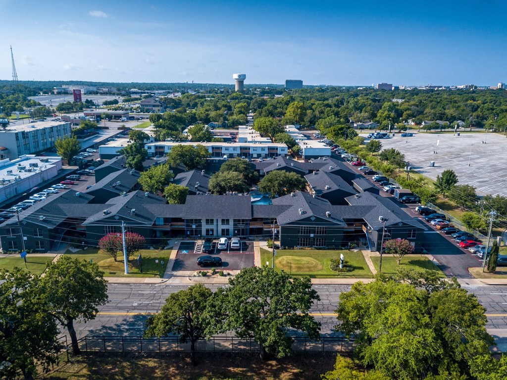 Aerial view of Studio 700 apartments in Arlington, Texas. The large, two story complex is surrounded by parking lots filled with cars.