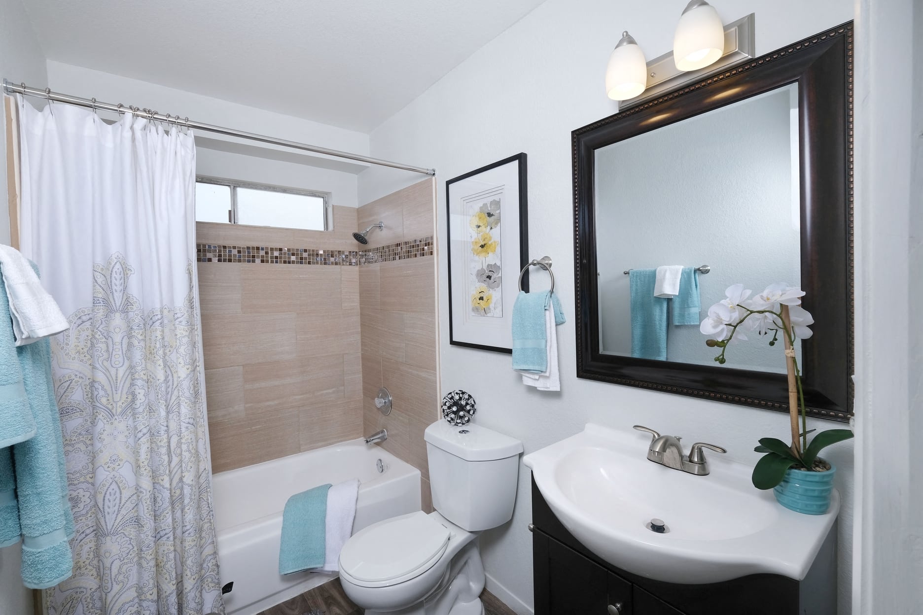Bathroom in one bedroom Fifteen 50 apartments Las Vegas with modern natural tile in bathtub shower and a dark framed mirror above a single sink.