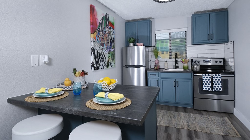Fusion Las Vegas apartment kitchen with blue cabinets with black pulls, electric stove, and stainless steel refrigerator.