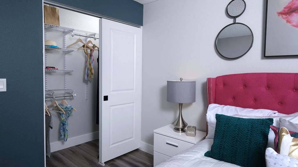 Fusion Las Vegas apartment closet white doors and built in wire shelving next to bed with hot pink headboard and teal crochet pillow.