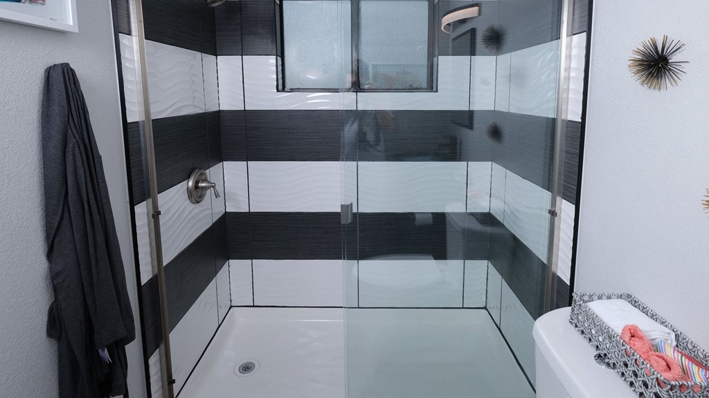 Fusion Las Vegas apartment shower with modern black and white tiles, black grout, sliding glass doors, and chrome plated fixtures.