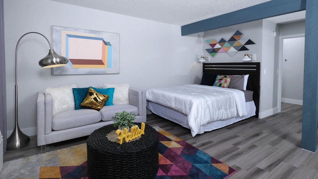 Fusion Las Vegas studio apartment with large bed, geometric wall hangings and paintings, and small couch with modern standing reading lamp.