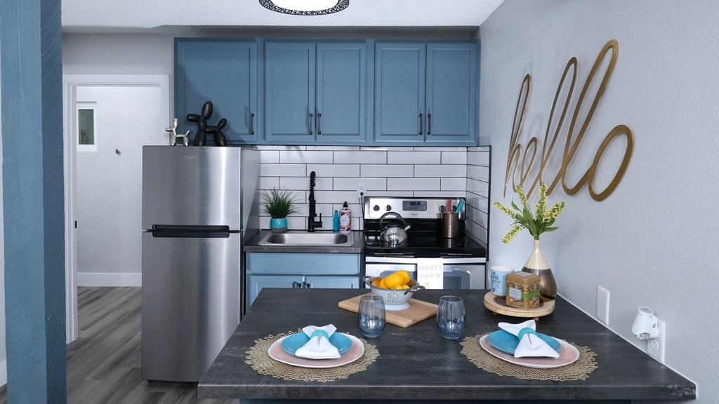 Fusion Las Vegas apartment kitchen with stainless steel appliances, navy blue cabinets, subway tile backsplash, and two place settings on island.