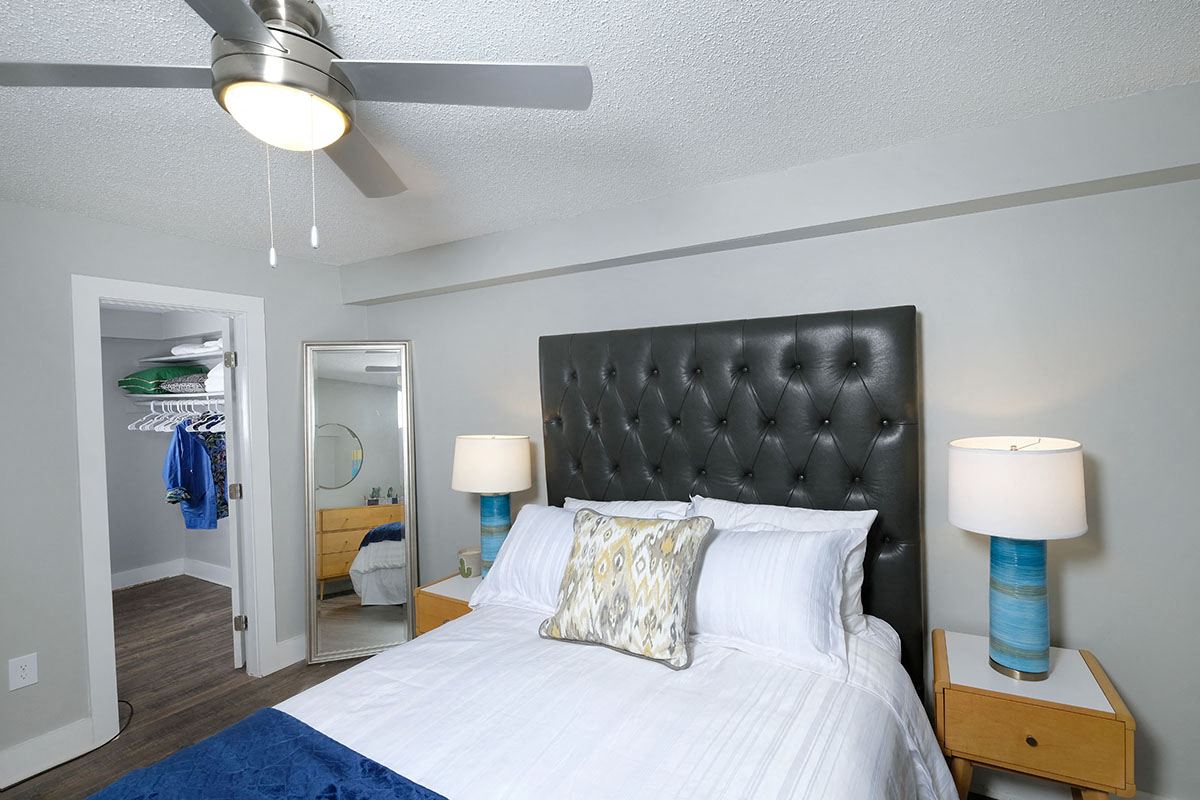 Bedroom in Mandarin Bay apartments in Jacksonville, FL with ceiling fan, walk-in closet, and large bed with leather headboard.