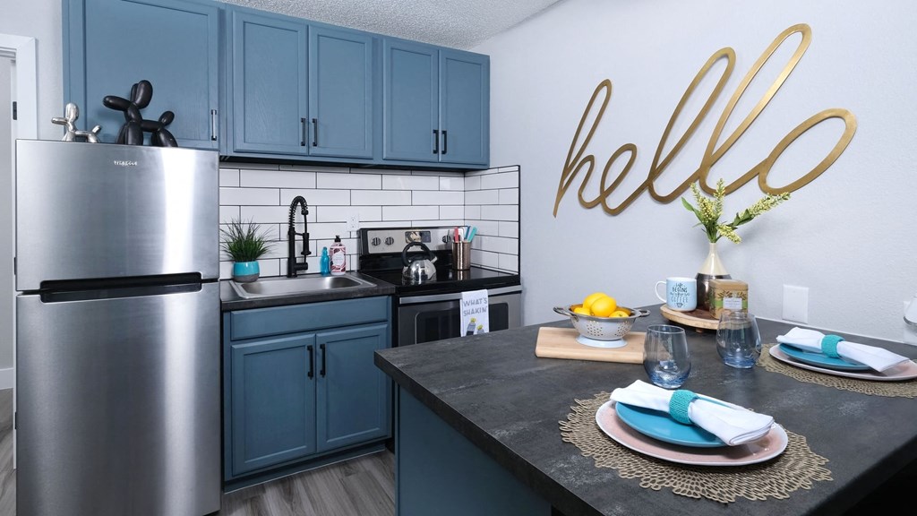 Fusion Las Vegas apartment kitchen with stainless steel electric stove and basin sink, and a large gold sign that reads "hello" in cursive.