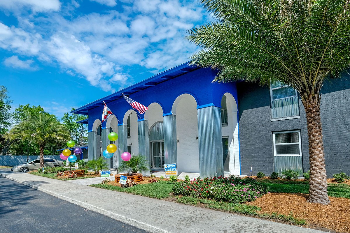 Jacksonville Mandarin Bay Apartments leasing office street view. Building is surrounded by grass and palm trees, balloons, and "Now Leasing" signs
