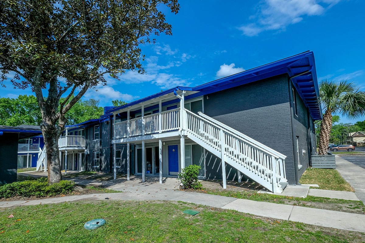 Jacksonville Mandarin Bay Apartments exterior shot. Building is two stories with blue-grey brick, blue roof, and white railed staircases
