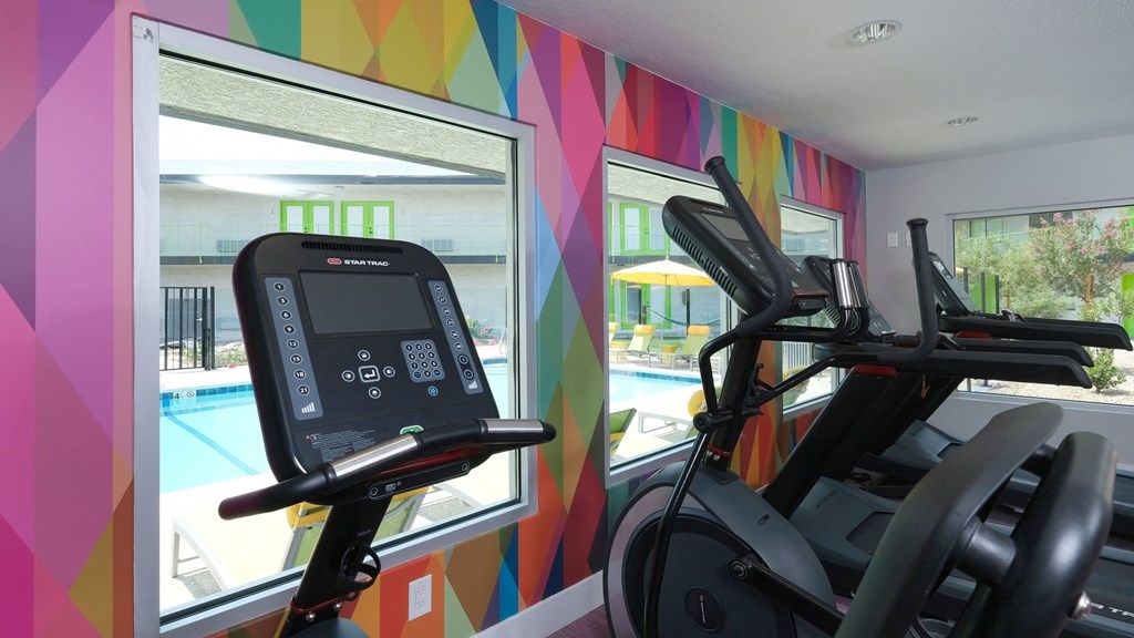 Fusion Las Vegas fitness center with colorful geometric wall and ellipticals looking out large windows toward community pool.