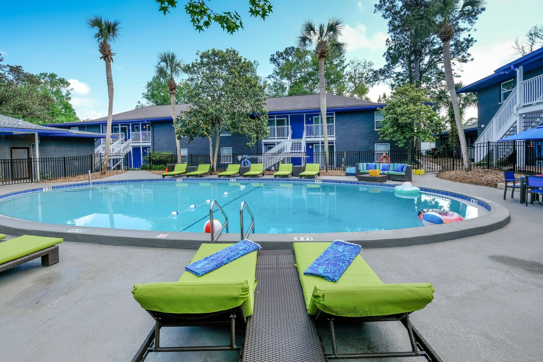 Mandarin Bay apartments round community pool with lime green loungers and large patio couches with blue and teal cushions.