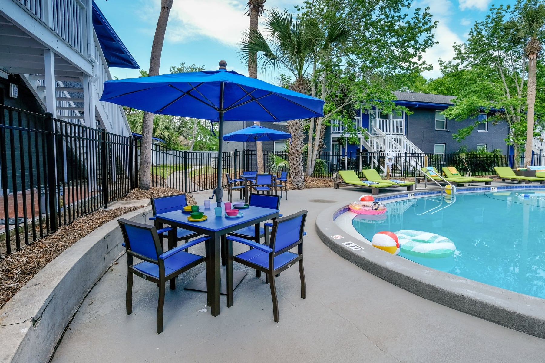 Blue patio tables and chairs with blue umbrellas next to community pool in Mandarin Bay apartments in Jacksonville, Florida.