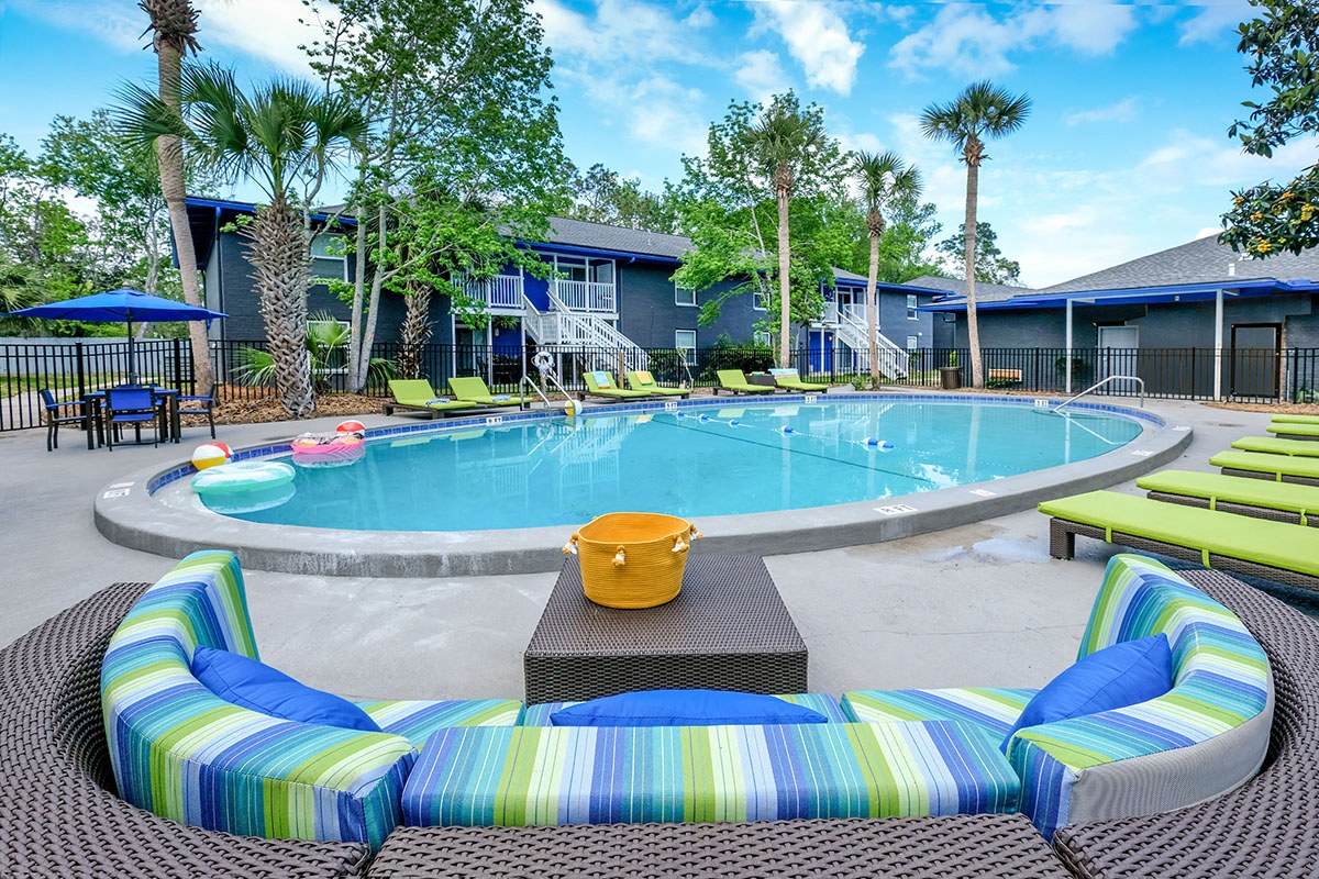 Mandarin Bay apartments round community pool with lime green loungers and a large green and blue striped patio couch with table.