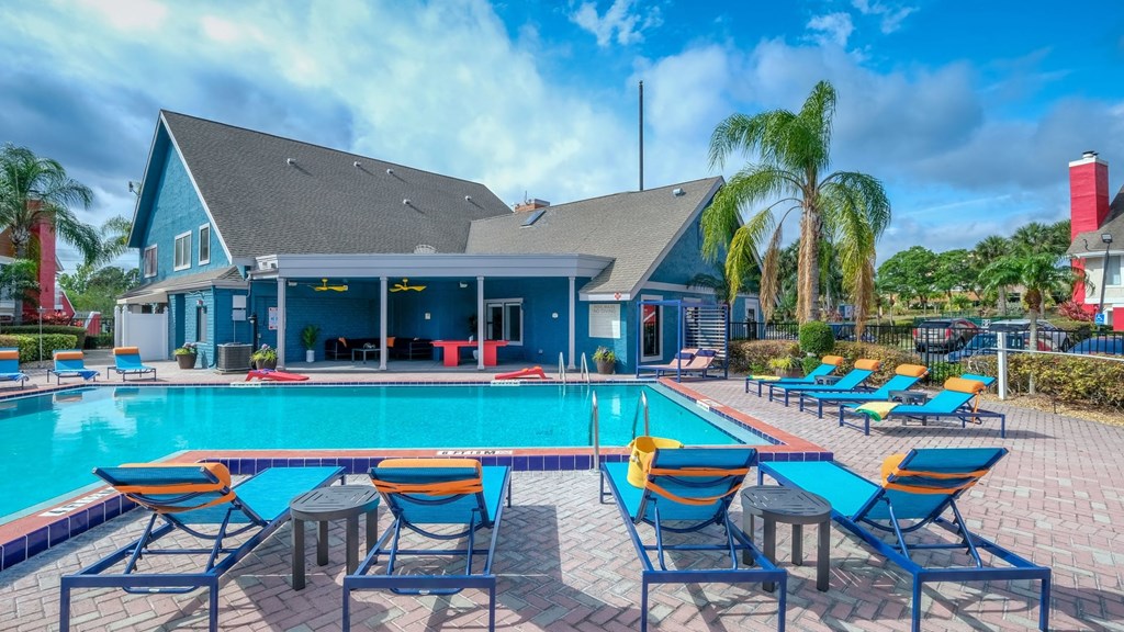 Fusion Orlando apartments community pool next to large pool house with covered patio, bright blue siding, and palm trees.