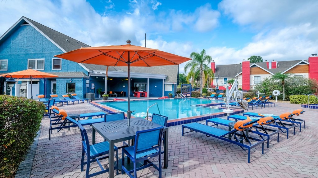 Fusion Orlando apartments community pool surrounded by blue patio lounge chairs and patio tables with bright orange umbrellas.