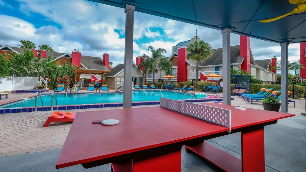 Fusion Orlando apartments poolside activities including ping pong table, corn hole, and bright blue lounge chairs.