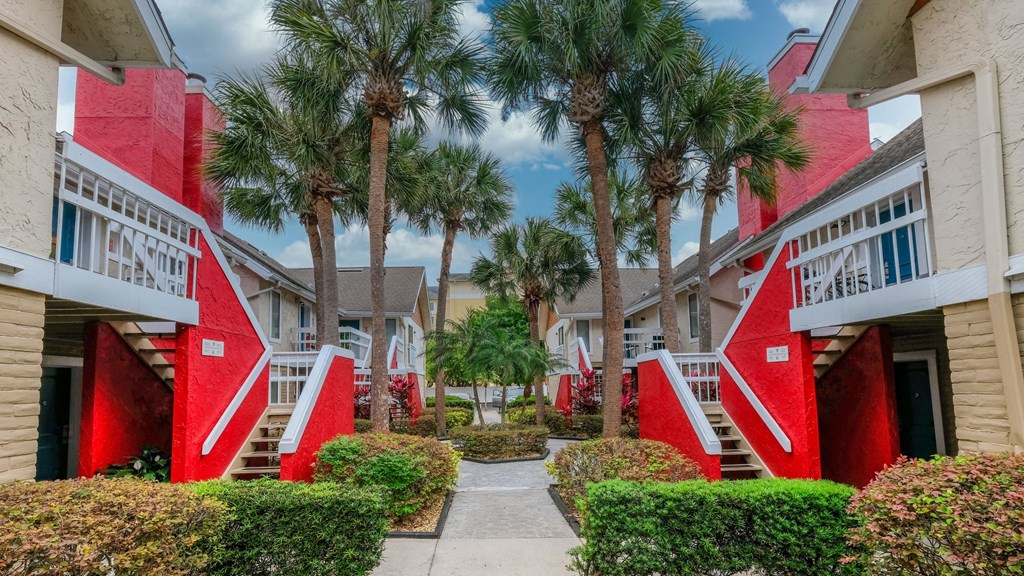 Fusion Orlando apartments exteriors with red staircases, blue front doors, and white railing on balconies. Center path is lined with palm trees.