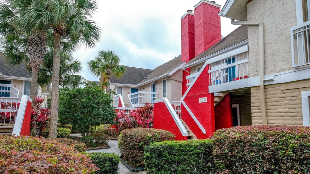 Two story Fusion Orlando apartments exteriors. Apartments have red staircases to second story and red chimneys, and tropical landscaping line paths.