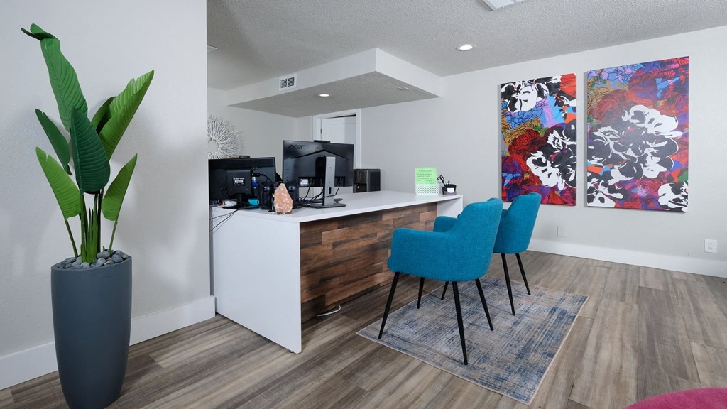 Fusion Orlando apartments leasing office with pallet wood reception desk, two blue modern chairs, and a modern floral painting on two canvases.