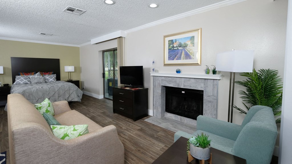 Fusion Orlando studio apartment spacious living area with built in fireplace, tan couch, teal sitting chair, and modern reading lamp.