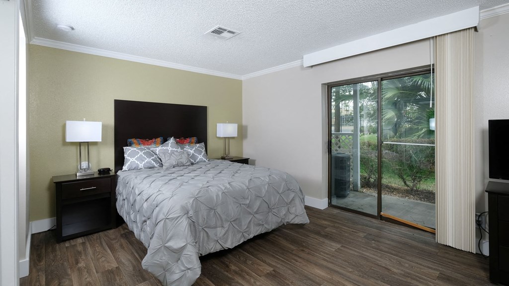Fusion Orlando furnished studio apartment bedroom with sliding glass door to tropical patio with palm trees. Bed is large with grey duvet.