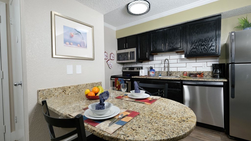 Fusion Orlando studio apartment kitchen with espresso cabinets and stainless steel microwave, electric stove, dishwasher, and fridge.